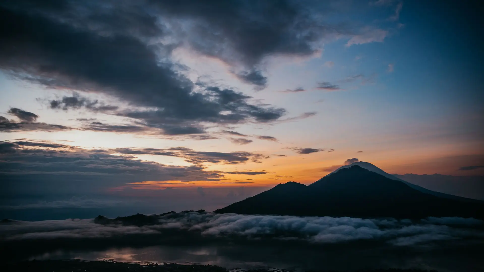 The outline of a volcano above a layer of low cloud at dusk
