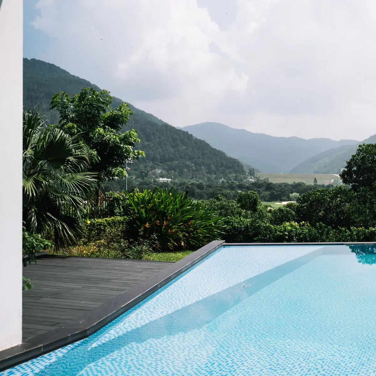 A swimming pool edged by a timber deck, with green hills beyond