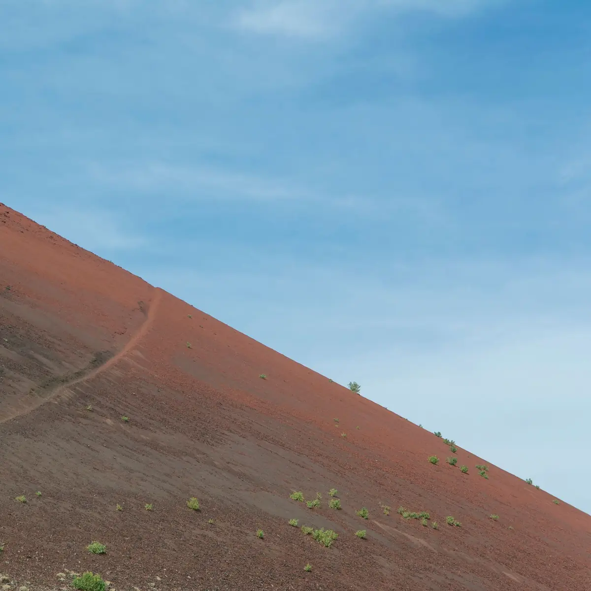 A narrow path climbing a bare volcanic slope under a blue sky